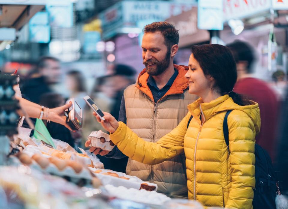 A couple makes a purchase with a smartphone at an outdoor market.