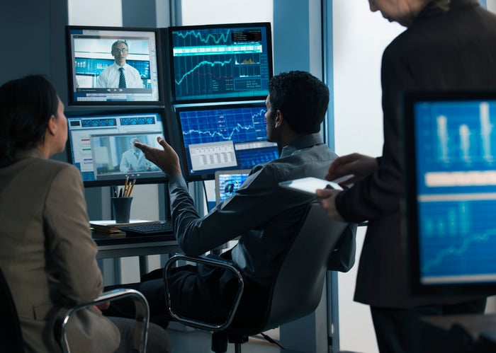 People participating in a video meeting in front of computers showing graphs.