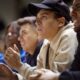 A young man anxiously watches a sporting event surrounded by a crowd of supporters all looking at a field. (Image Credits: Lighthouse Films/Getty Images)