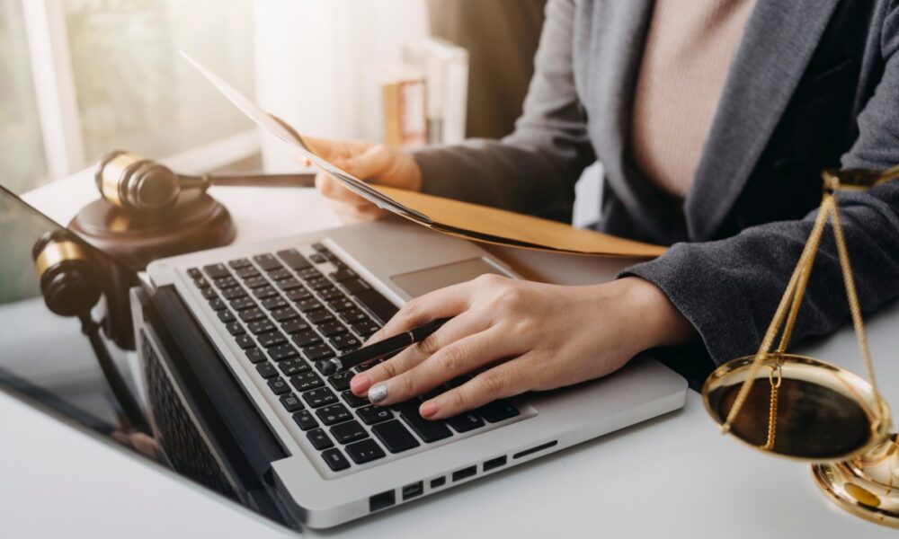 Woman at a desk with a laptop, brass scales and gavel representing the legal system