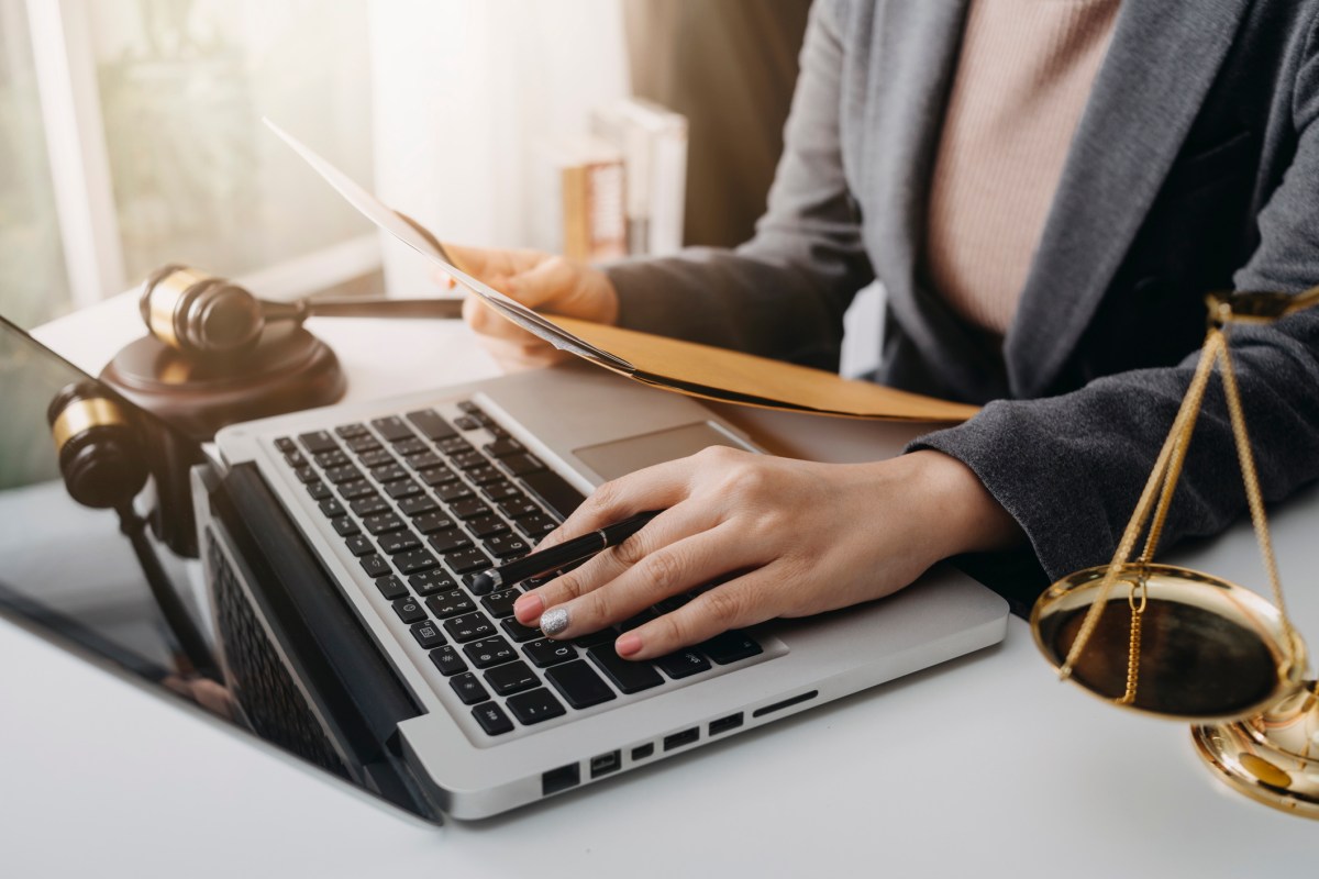 Woman at a desk with a laptop, brass scales and gavel representing the legal system